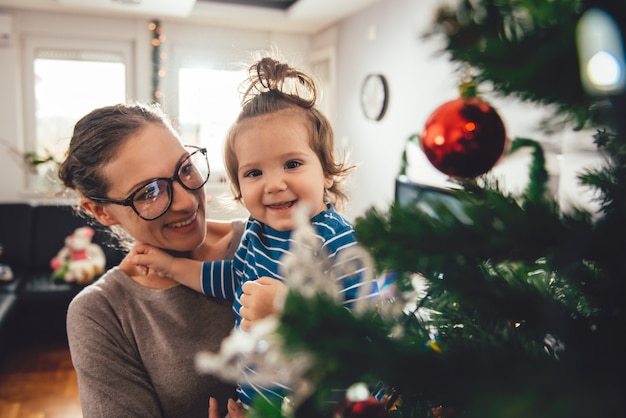 Mother holding daughter and decorating christmas tree