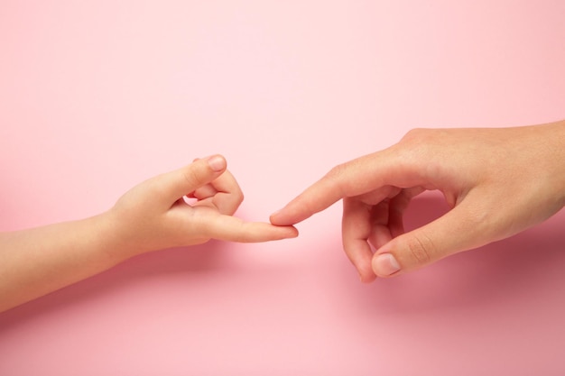 Mother holding daughter hand on pink background