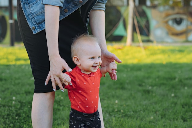 Mother holding hand of baby daughter supporting child making first steps