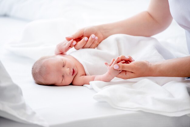 Mother holding hands of her sleeping newborn baby daughter in the bed