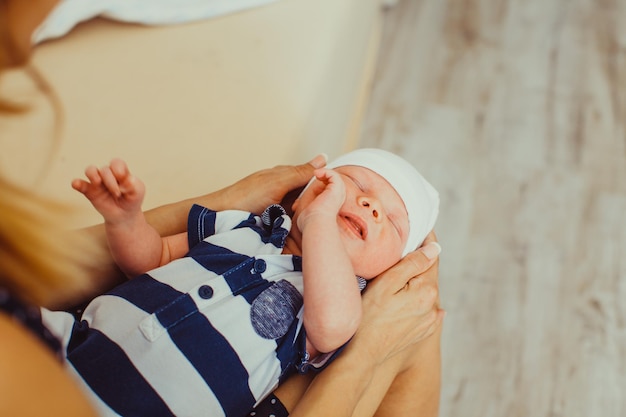 Mother holding her baby in stripped clothing in hands on her knees