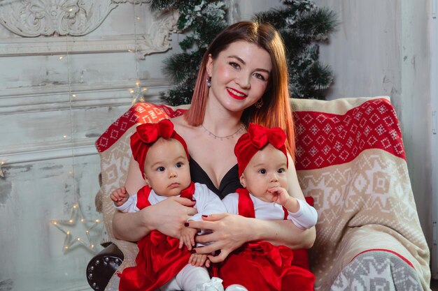 Mother holding identical twin babies in red dresses