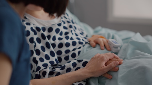 Mother holding sick daughter hands after sufffering medical surgery during recovery examination