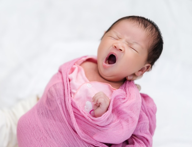 Mother holding sleepy newborn baby yawning in her arm