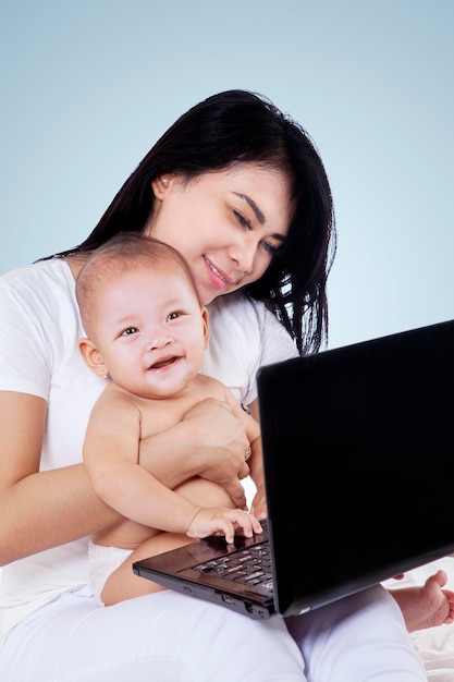 Mother holds her baby while using a laptop on studio