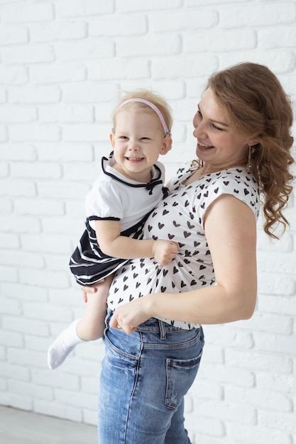 Mother holds her child with hearing aids and cochlear implants on white brick wall Deaf and health concept