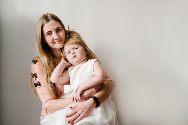 The mother holds on his hands little girl on light background indoor Portrait of mom and daughter sitting in home The concept of happy family holiday woman's day Mother's Day