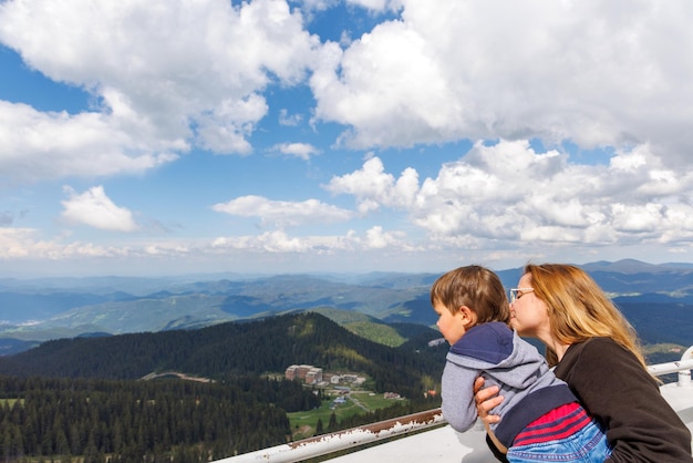 Mother holds son and shows him landscapes of forest valley of Rhodope Mountains while standing on tower of Snezhan