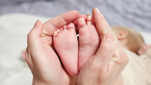 Mother holds tiny pink feet of newborn daughter on bed