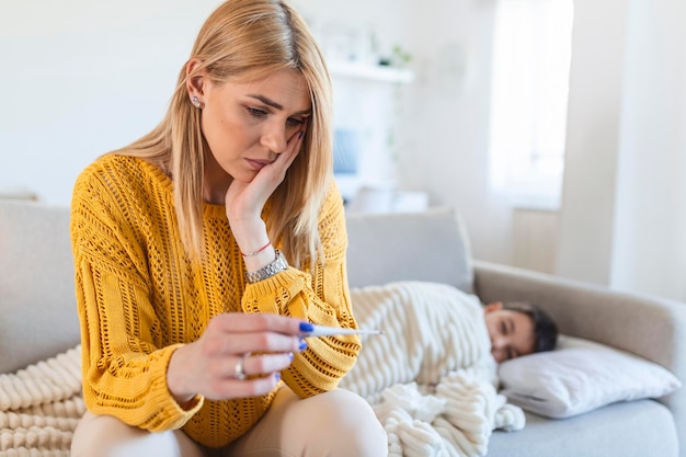 Mother at home and measure a temperature on her sick child Sick little boy sitting on bed The boy has a head ache and fever The mother is comforting the boy