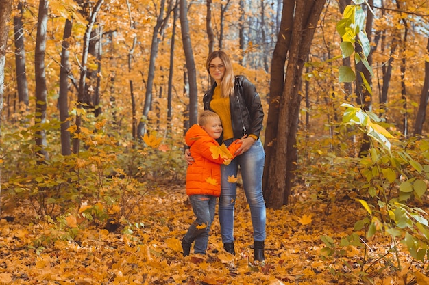 Mother hugging her child during walk in autumn park. Fall season and single parent concept.