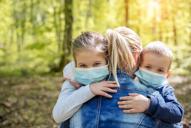 Foto madre che abbraccia i suoi figli che indossano maschere mediche per proteggersi dal virus covid-19