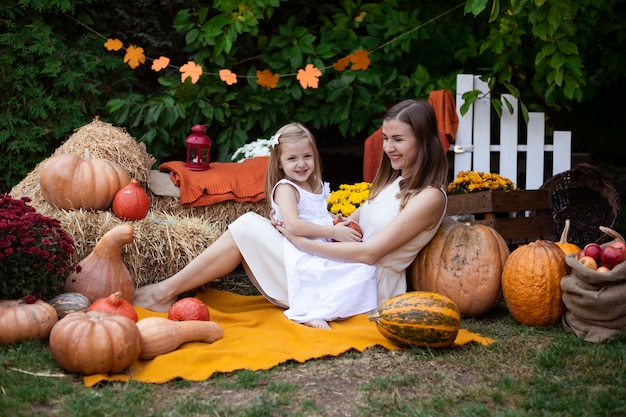 Mother hugging her daughter in autumn background with pumpkins