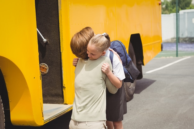 Foto madre che abbraccia sua figlia con lo scuolabus