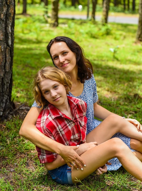 Photo mother hugging her little daughter resting on her sholder against of green grass in the forest