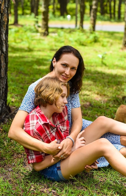 Foto madre che abbraccia la sua piccola figlia appoggiata sul suo sholder con gli occhi chiusi contro l'erba verde dentro