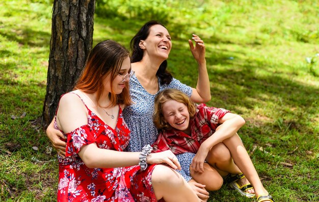 Mother hugging her teenage daughter and little daughter and laughin together with them in the forest