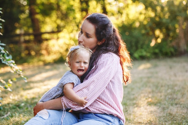 Mother hugging pacifying sad upset crying toddler girl family young mom and crying baby in park