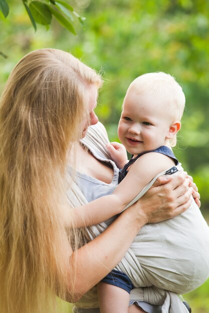 Mother is carrying her child and walking. Baby in sling outdoor.