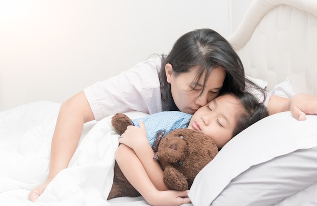 Mother is kissing her daughter in cheek while laying on bed 