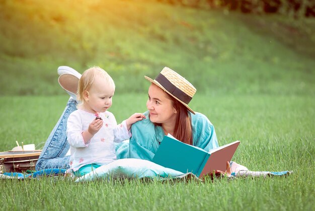 母は公園の芝生の上に横たわっている女の赤ちゃんのための本を読んでいます