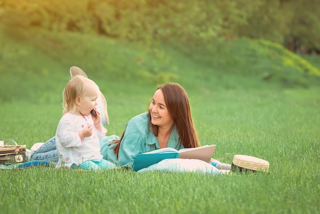 Mother is reading book for baby girl lying on the grass in the park