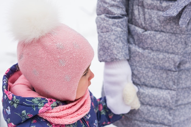 Mother is walking with her little daughter in snowy forest