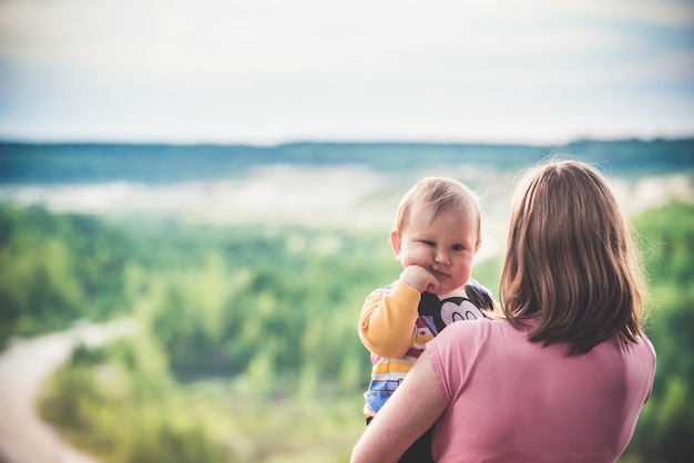 Mother keeps the baby on his hands against the background of nature