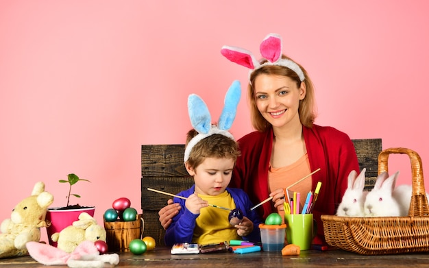 Мать и ребенок рисуют пасхальные яйца, ребенок держит корзину с крашеными яйцами
