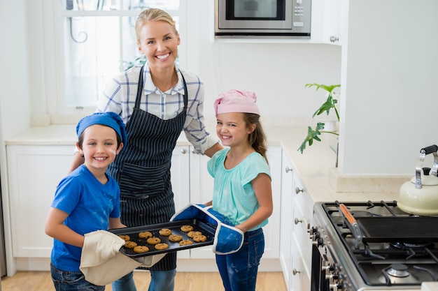 Mother and kids holding tray of baked cookies in kitchen