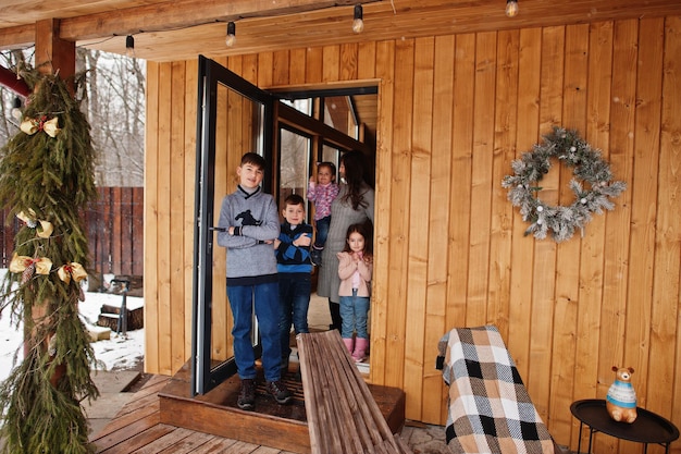 Mother and kids in modern wooden house stand near door entrance