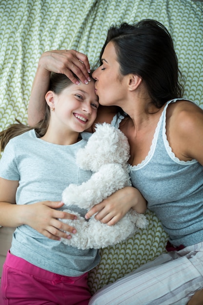 Mother kissing on daughter forehead on bed