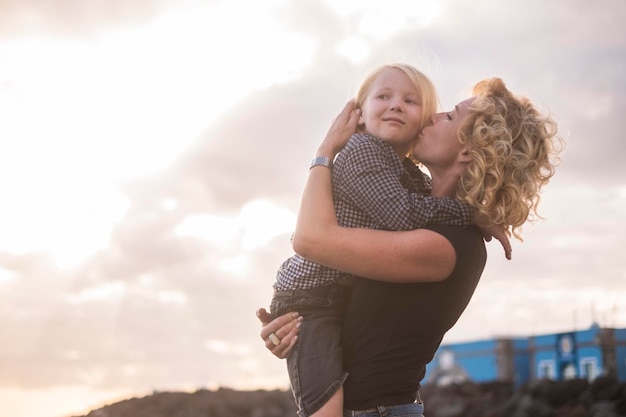 mother kissing daughter while standing against cloudy sky during sunset