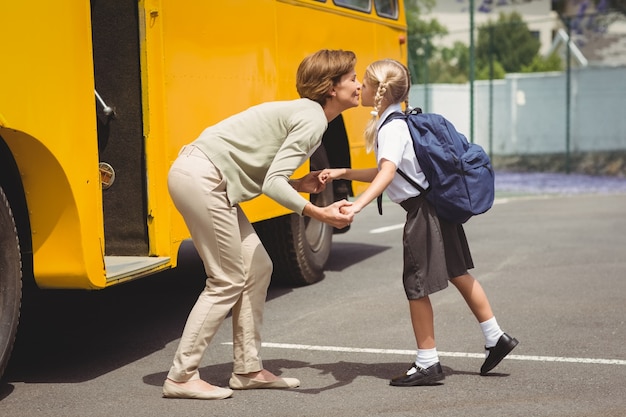 Mother kissing her daughter by school bus