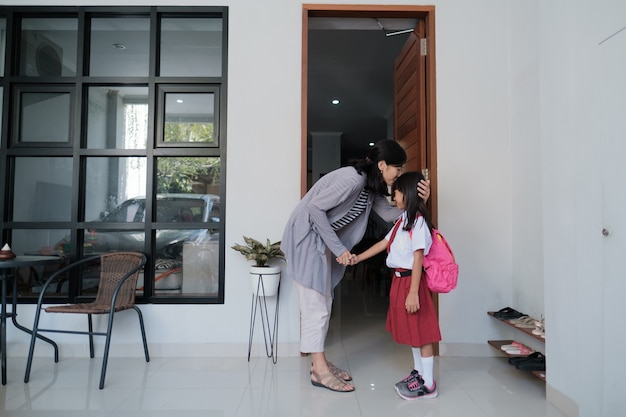 그녀를 학교에 데려 가기 전에 그녀의 딸 이마에 키스하는 어머니. 제복을 입은 아시아 학생