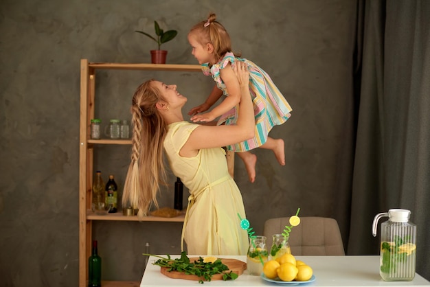 Mother and little daughter make summer lemon drink at kitchen woman toss little girl