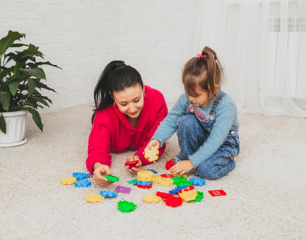 Mother and little daughter play constructor on the carpet in the living room. happy family