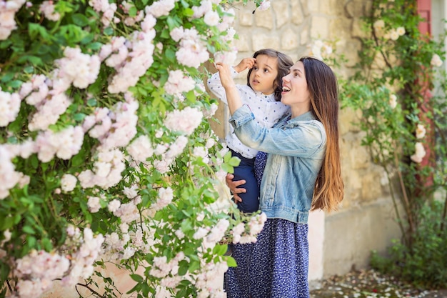 Madre e piccolo neonato bello che esaminano il cespuglio con le rose bianche