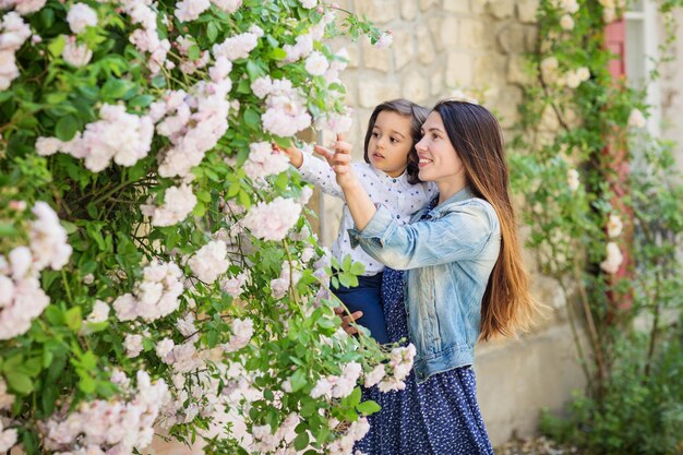 白いバラの茂みを見ている母と小さなハンサムな男の子