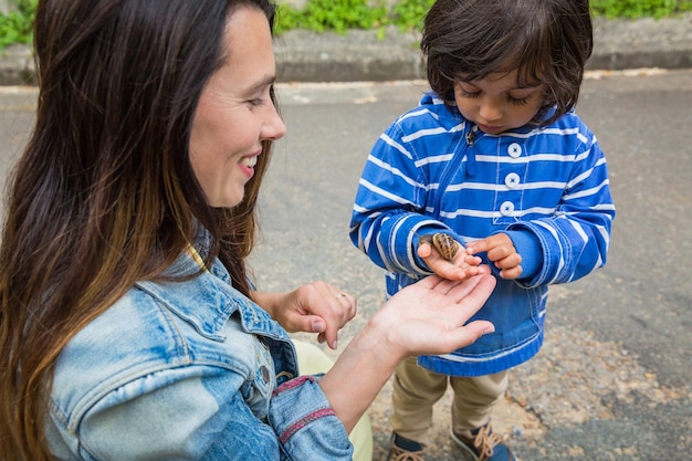 Mother and little handsome baby boy playing outdoor with a snail