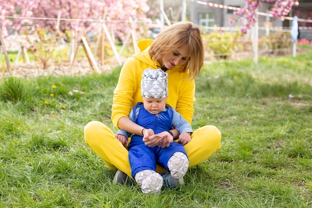 어머니와 어린 아들은 꽃이 만발한 사쿠라 정원에서 즐거운 시간을 보내고 있습니다. 초상화 여자는 작은 아기를 껴안고