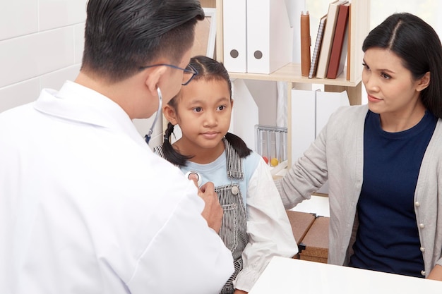 Mother looking at doctor examining girl in clinic