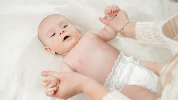 Photo mother making massage and gymnastics to her little baby boy lying on bed concept of parenting baby