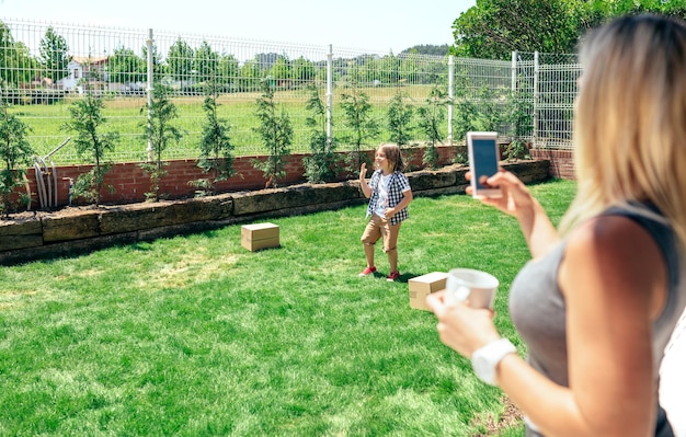 Mother making a mobile photo of her son while playing in the garden Background focus on child