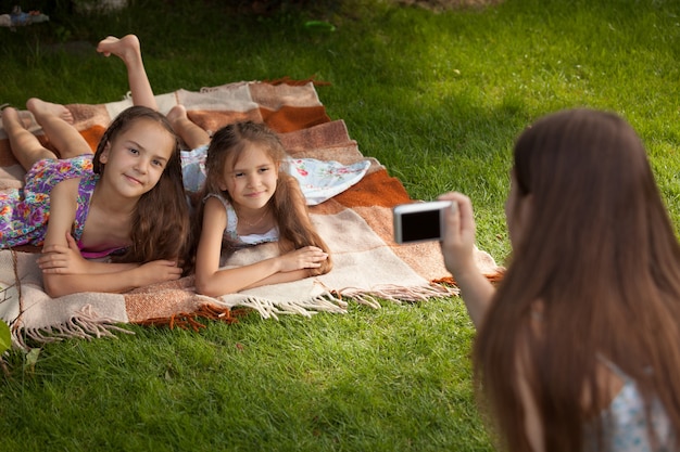 Mother making photo of two little girls lying on grass