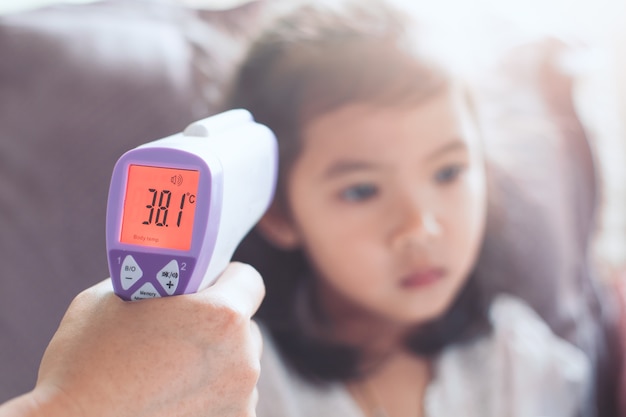 Mother measuring temperature her sick asian little child girl with infrared thermometer