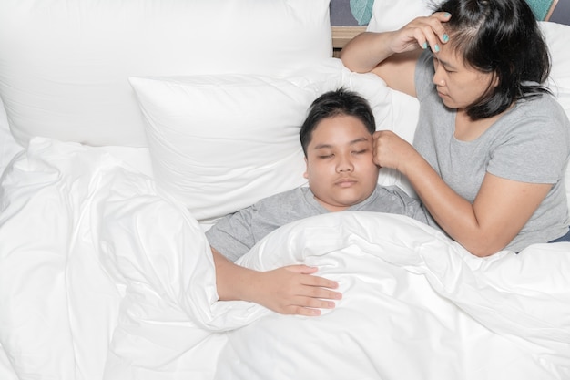 病気の子供の体温を測定している母親。ベッドに横たわっている高熱と母親がストレスを感じる病気の子供、ヘルスケアの概念。