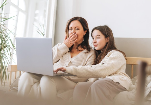 Mother middle aged woman and daughter teenager using laptop together in the light interior