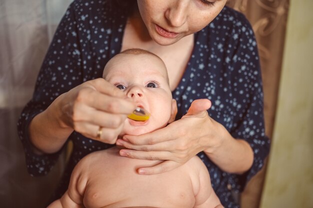 母親と新生児の面白い感情的な泣いている幼児の裸の男の子は、薬液を服用するか、