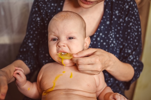 Mother and newborn funny emotional crying infant naked baby boy takes liquid medication or